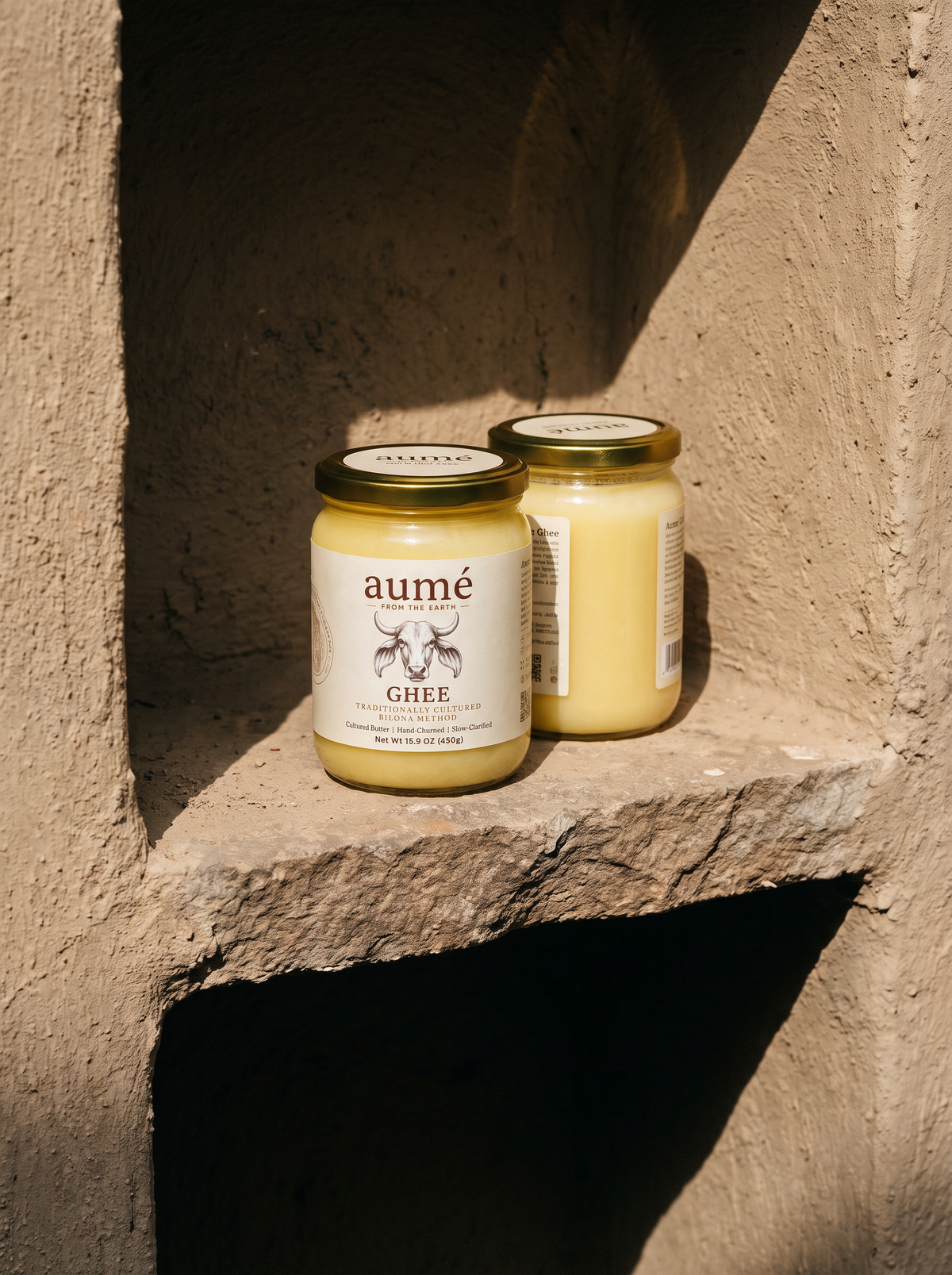 Two jars of Aumé A2 Gir cow bilona ghee on a stone ledge in warm sunlight